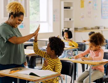 A teacher giving a student a high five in a classroom.