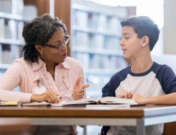 An educator helping a middle school student in a library.