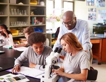 A teacher helping high school students use a microscope.