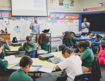 A teacher presenting a lesson while a student teacher watches.