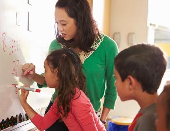 Teacher helping a student with an equation on a whiteboard.