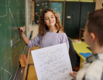 A middle school student working on a math equation on a blackboard.