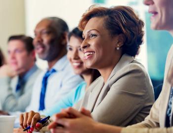 A smiling woman sits at a conference table with others.