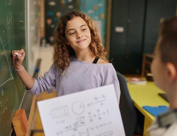 Two students working on a math equation on a blackboard.