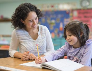A teacher assists an elementary student with an assignment in a classroom.