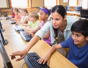 A teacher assists a middle school student in a computer class.