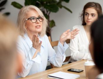 A woman seated at a table having a discussion with peers.