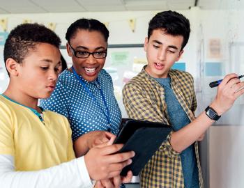 Three middle school students work on a math equation at a whiteboard.